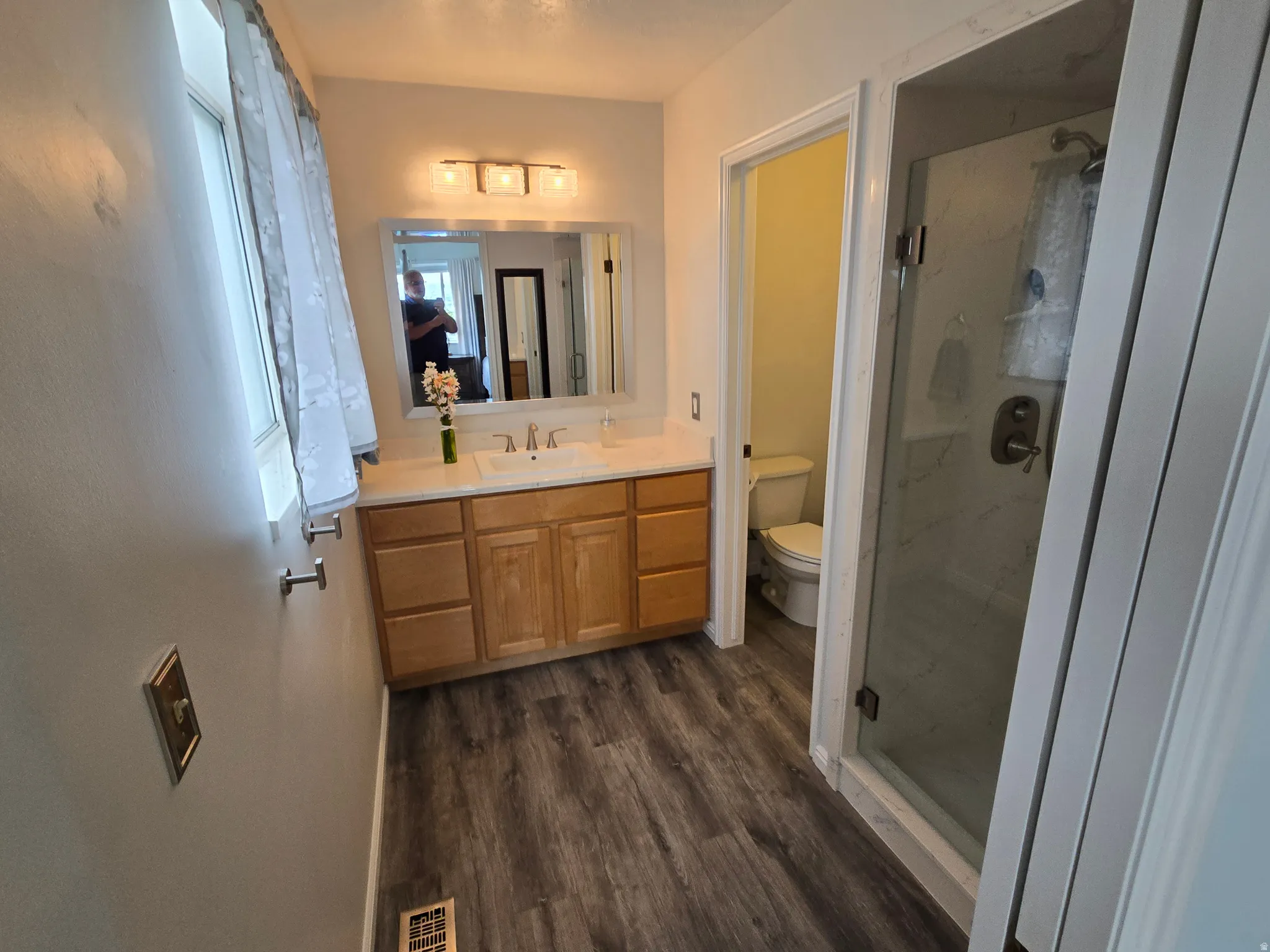 Bathroom featuring wood-finish flooring, a light wood vanity with a white countertop, and a shower enclosure with a glass door