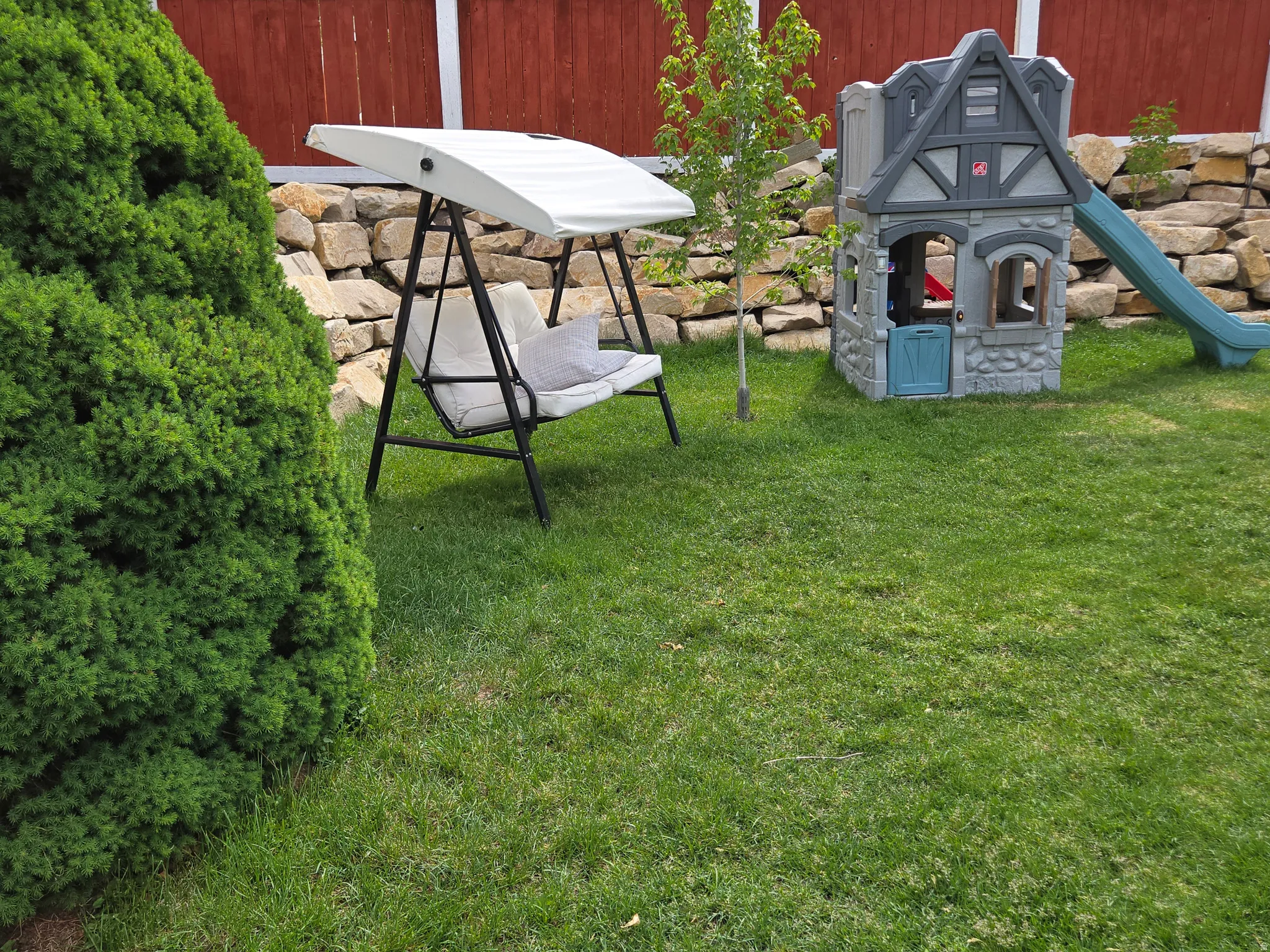 Lush green lawn with a stone retaining wall and a wood fence