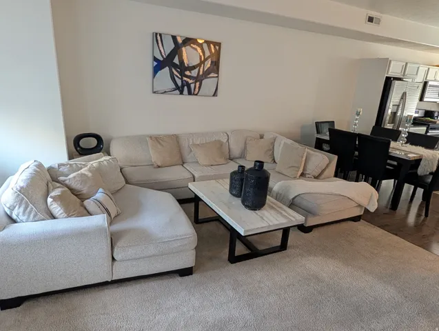 Open-concept living area featuring light-toned carpeting, a durable marble-finish coffee table with a dark metal base, and recessed lighting