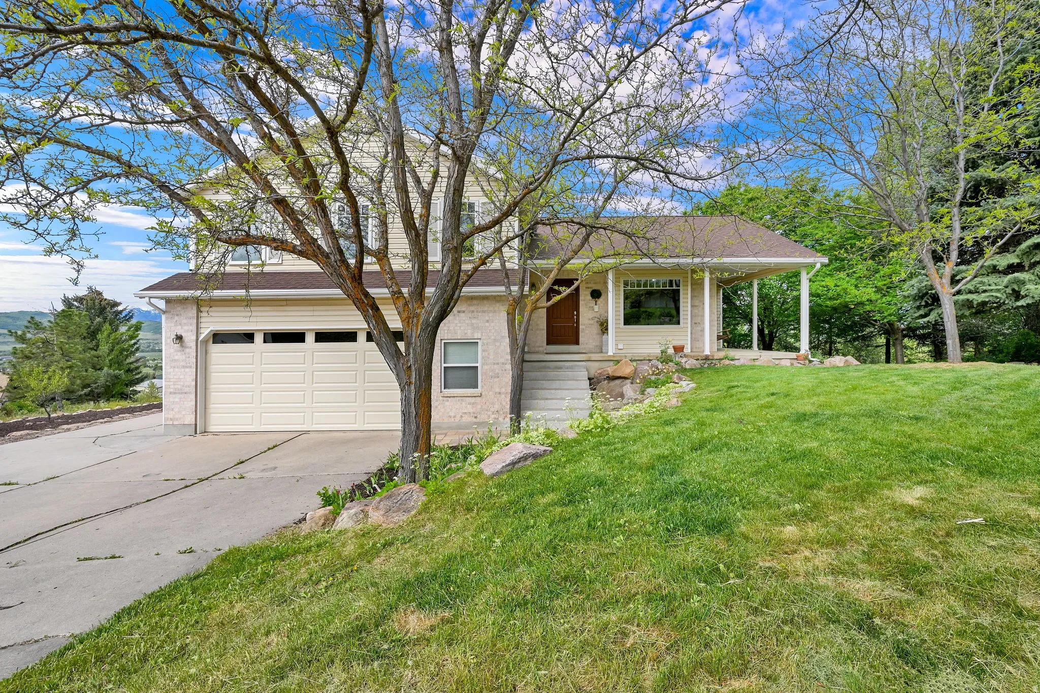 Two-story residence featuring a two-car garage, covered porch, concrete driveway, and mature landscaping