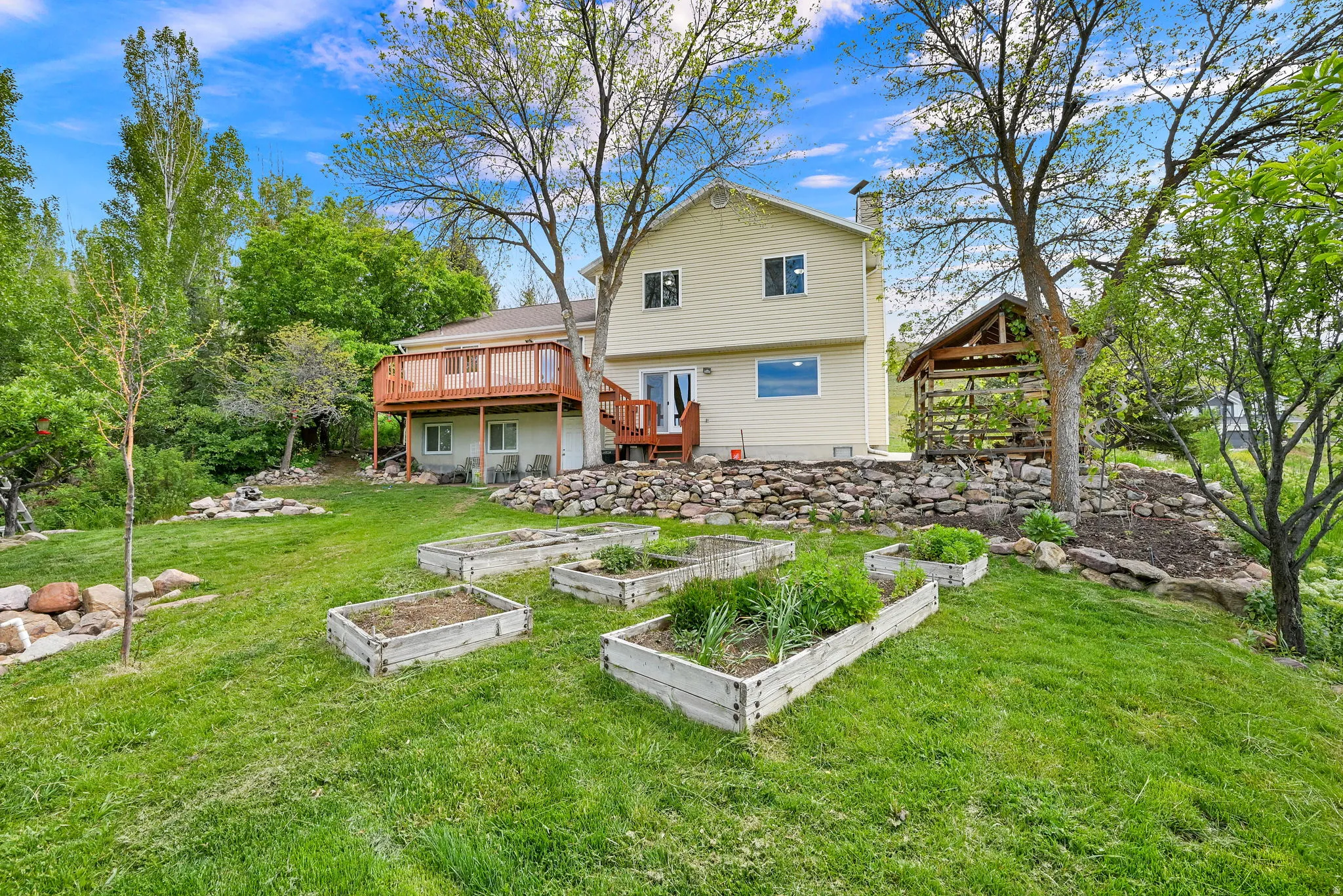 Expansive rear yard featuring multiple raised garden beds, a two-story residence with a second-story deck, a ground-level patio, and a separate gazebo structure
