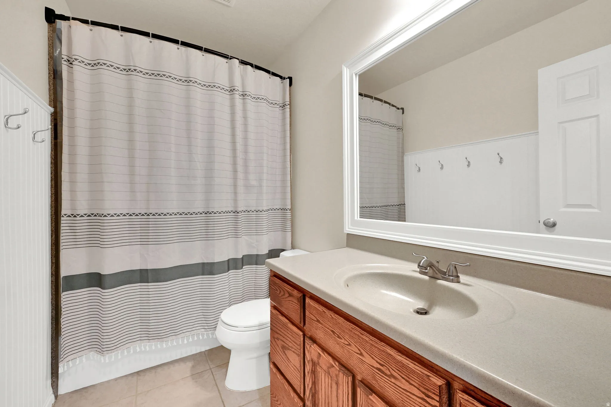 Bathroom featuring a wood-finish vanity with a built-in sink, a framed mirror, and beadboard wainscoting