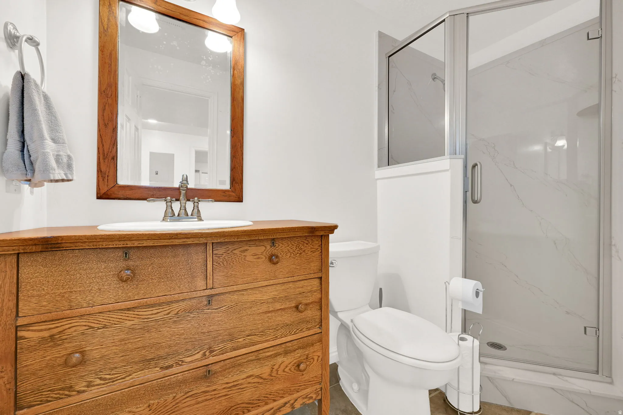 Bathroom featuring a custom wood-finish vanity with an integrated sink, a framed mirror, and a glass-enclosed shower with white tiled walls