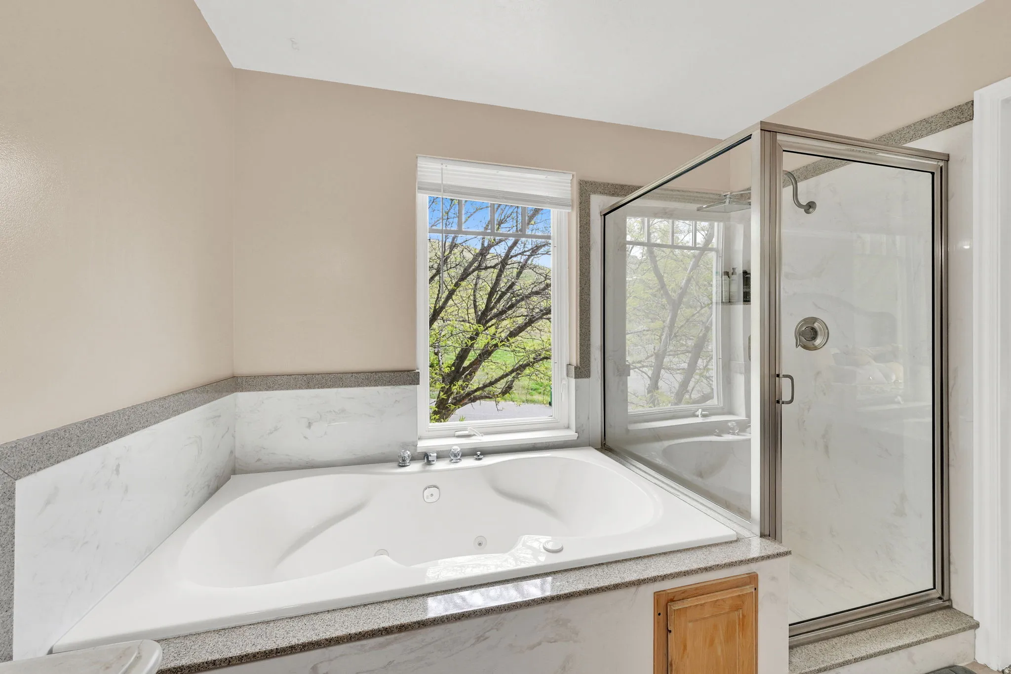 Corner jetted tub set within a marble surround with a granular countertop