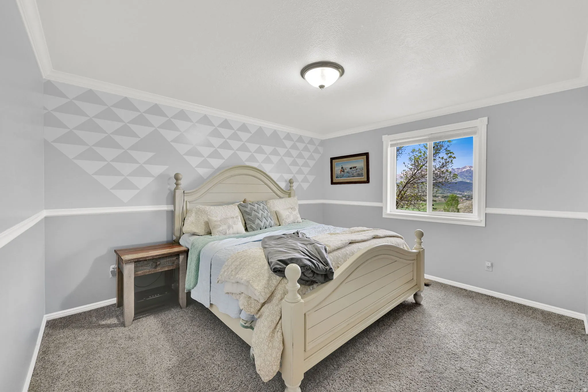 Carpeted room with a geometric accent wall featuring a chair rail, crown molding, and a window framing a mountainous landscape