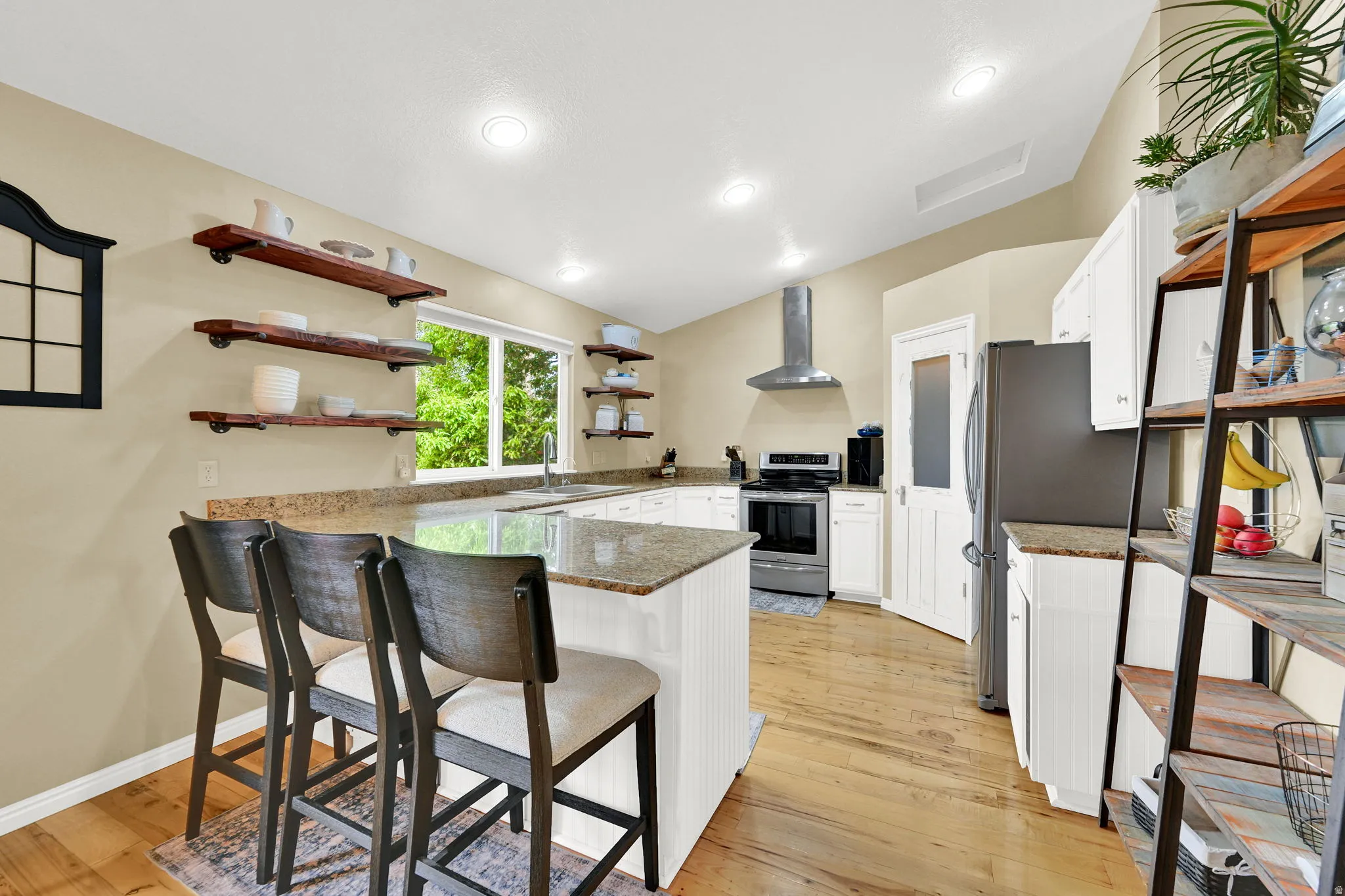 Kitchen featuring a granite-topped island with seating, white cabinetry, stainless steel appliances, wood-finish flooring, and recessed lighting