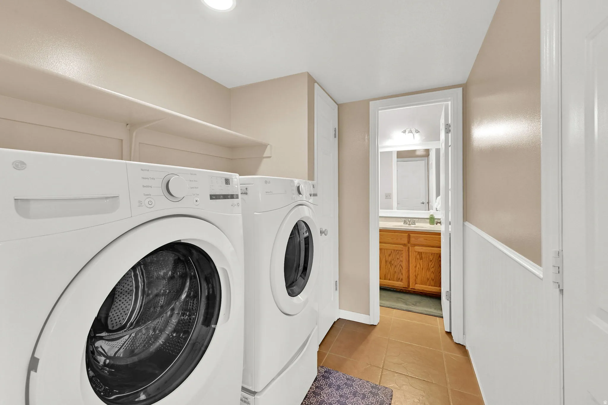 Dedicated laundry area featuring a front-loading washer and dryer, overhead shelving, and recessed lighting