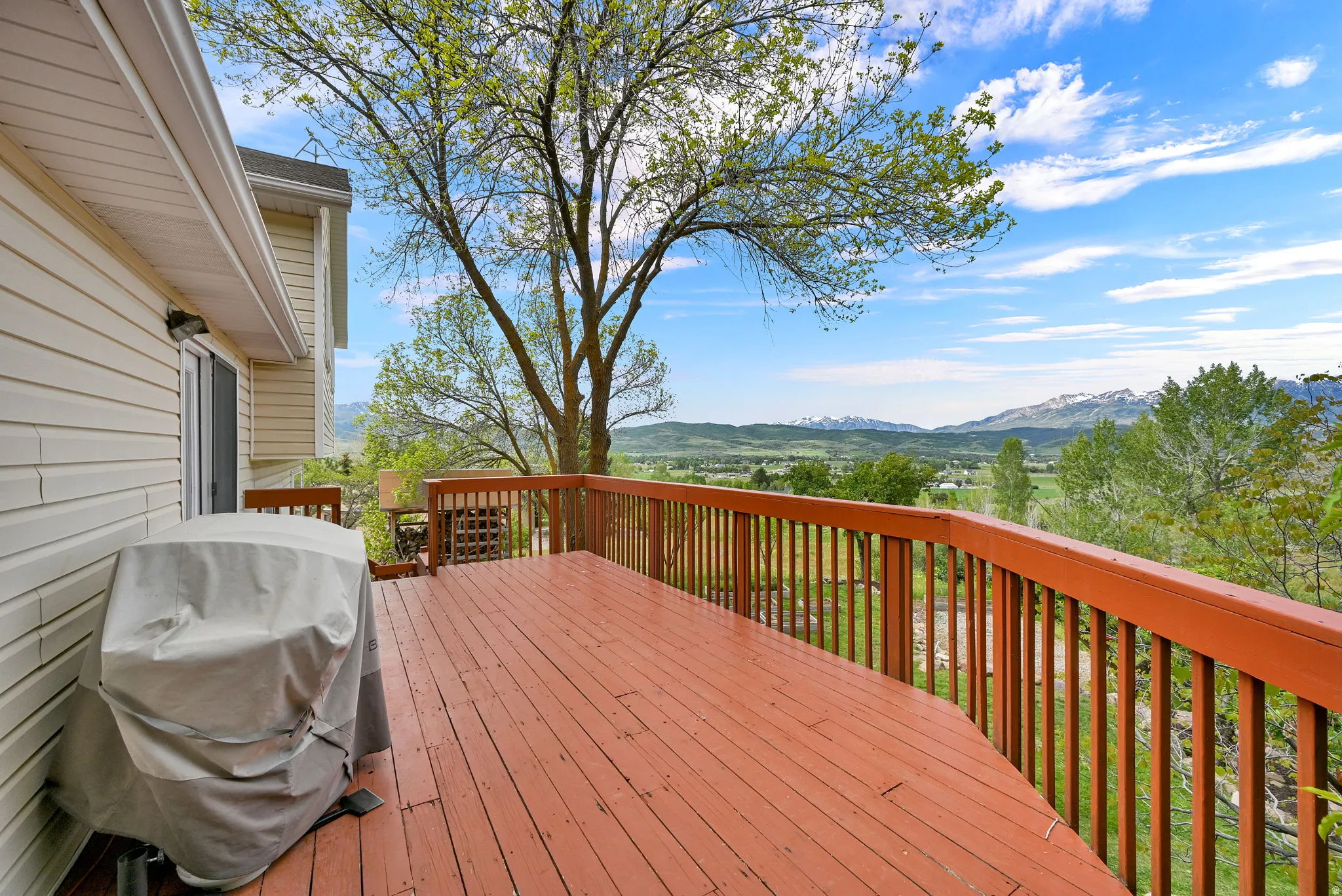 Expansive outdoor deck featuring wood flooring and railings, overlooking distant mountains and green landscapes