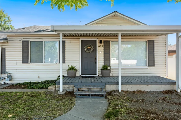 Exterior featuring light-toned horizontal siding, a dark entry door, and a covered porch with a dark-stained deck