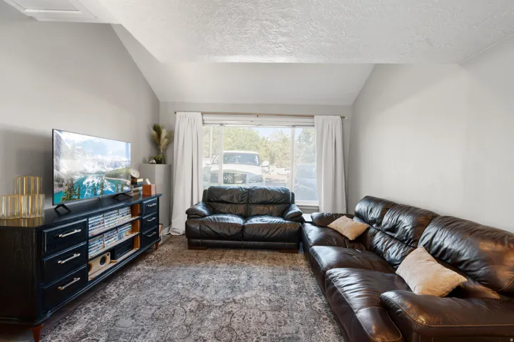 Living area featuring vaulted ceilings, light gray wall paint, and a large window