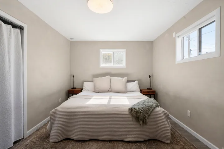 Bedroom featuring wood-finish flooring, neutral wall tones, and two windows providing natural light