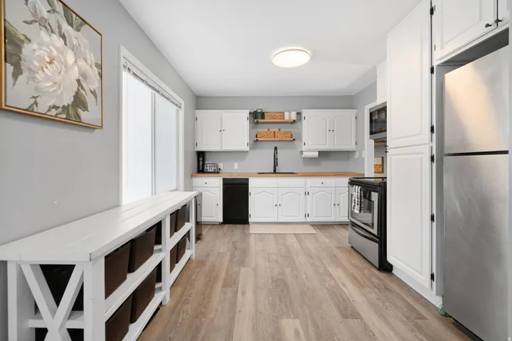 Kitchen featuring wood-finish flooring, white cabinetry, light countertops, and a full suite of stainless steel and black appliances