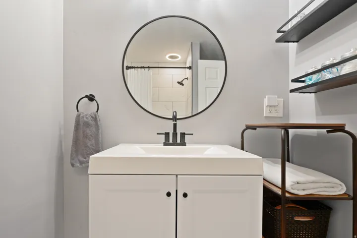 Bathroom vanity with integrated sink, matte black faucet, and round framed mirror