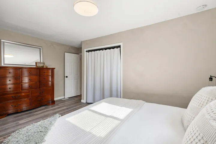 Bedroom featuring light gray wall paint, wood-finish flooring, a white paneled door, and a closet with a white curtain
