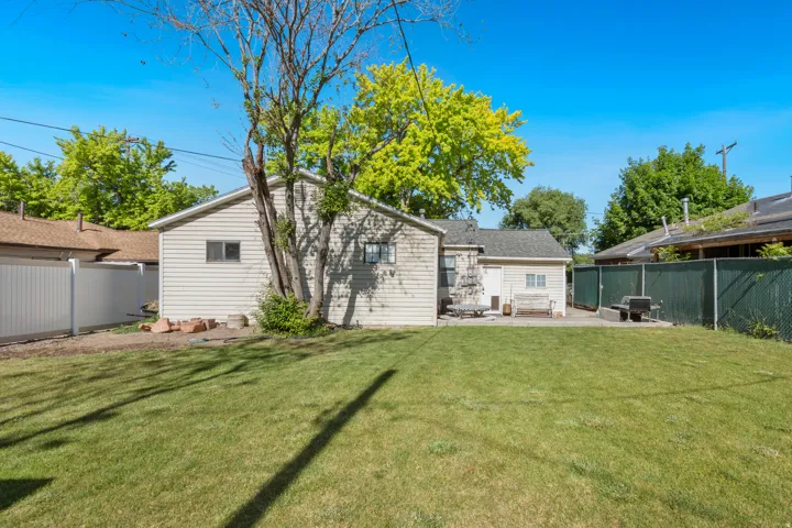 Expansive green lawn with a mature tree, bordered by a white privacy fence and a chain-link fence