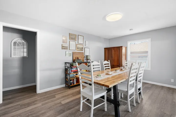 Dining area featuring wood-finish flooring, light gray wall paint, white trim, and a window providing natural light