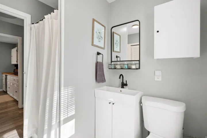 Bathroom featuring a white vanity with integrated sink, black-framed mirror with lower shelf, and a white wall-mounted cabinet
