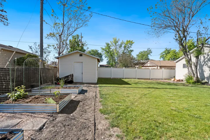Expansive backyard featuring a manicured lawn, white vinyl fencing, and a dedicated garden area with multiple raised beds