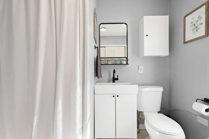 Bathroom featuring a white shower curtain, vanity with integrated sink, matte black faucet, wall-mounted storage cabinet, and toilet