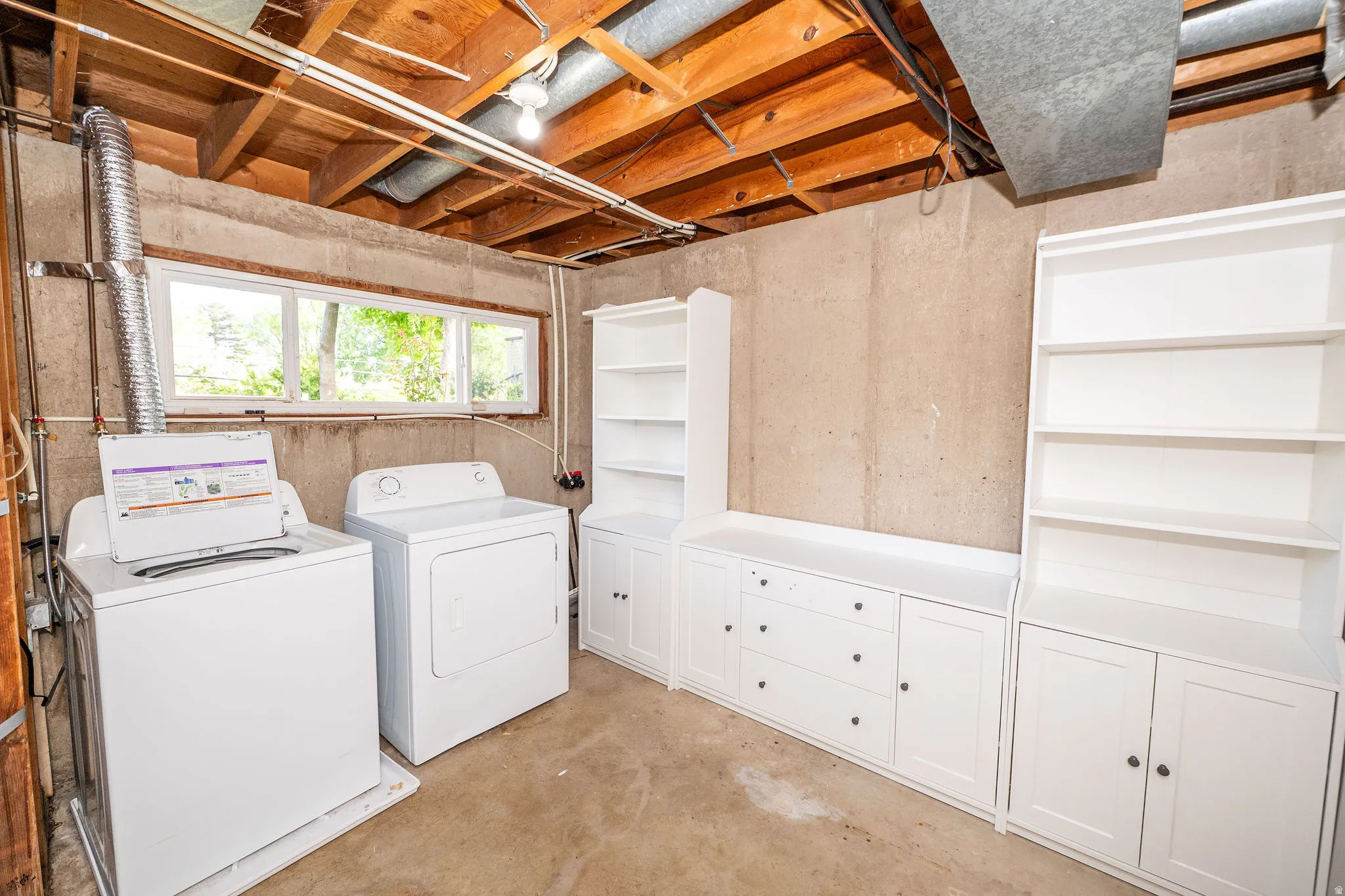 Laundry area with built-in white cabinetry, open shelving, and a concrete floor