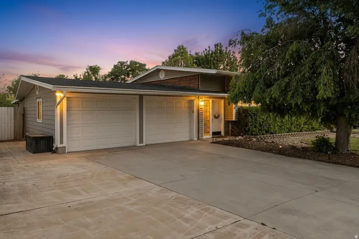 Split-level residence featuring gray siding, a two-car garage with white paneled doors, and a concrete driveway