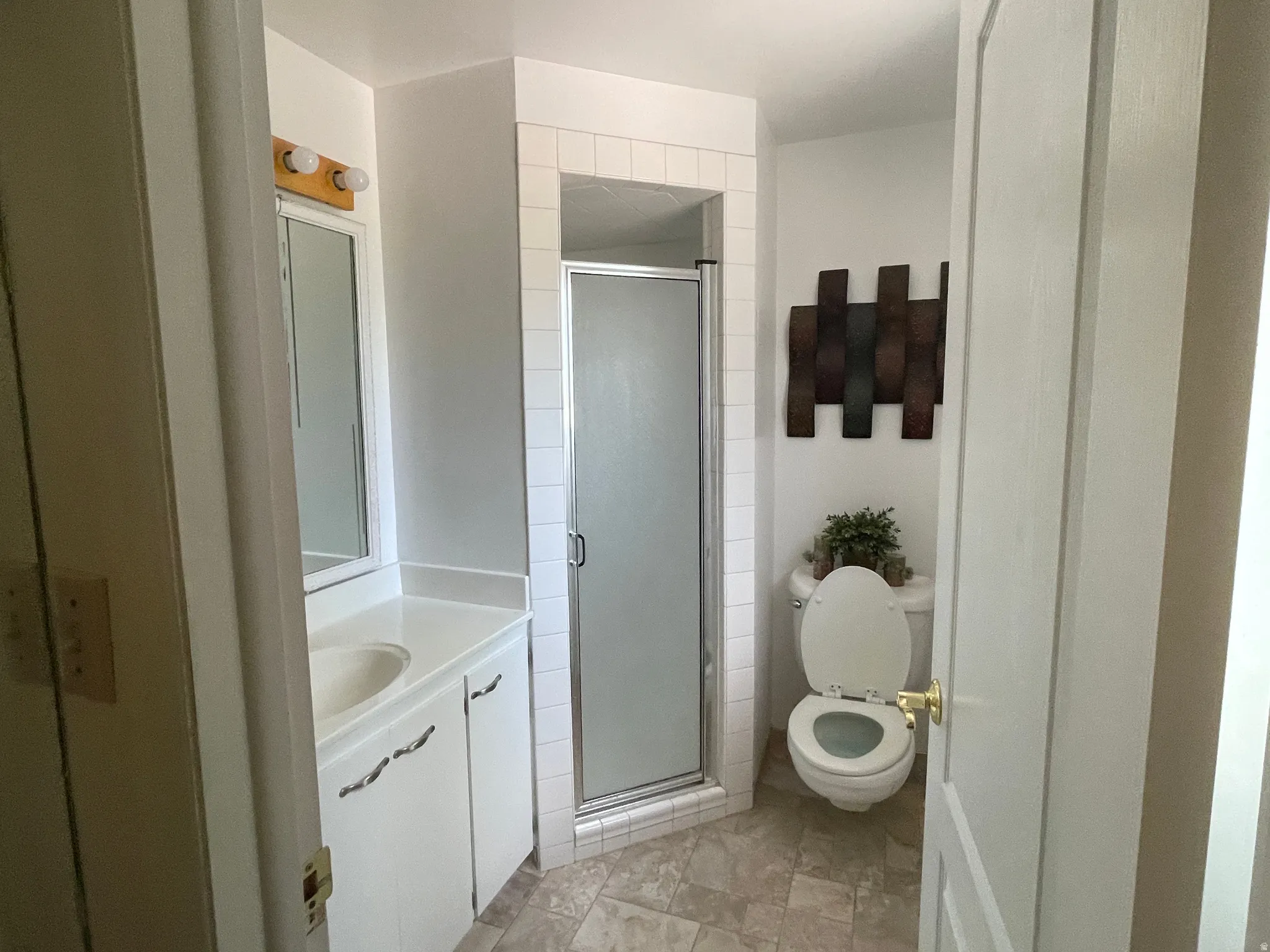 Full bathroom featuring a white vanity with integrated sink, a mirrored medicine cabinet, a corner shower with a glass enclosure, and a commode