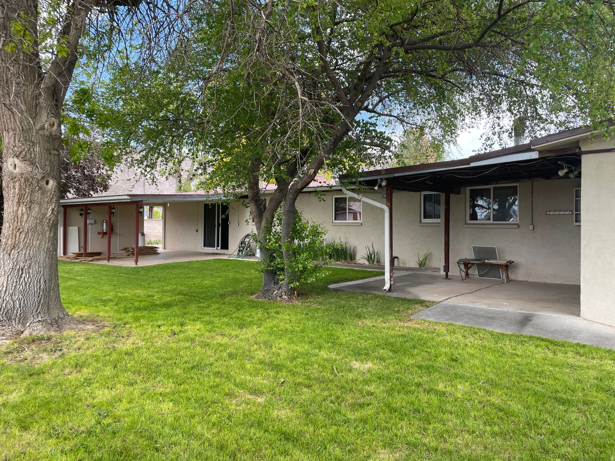 Expansive green lawn with mature shade trees, and two covered concrete patios