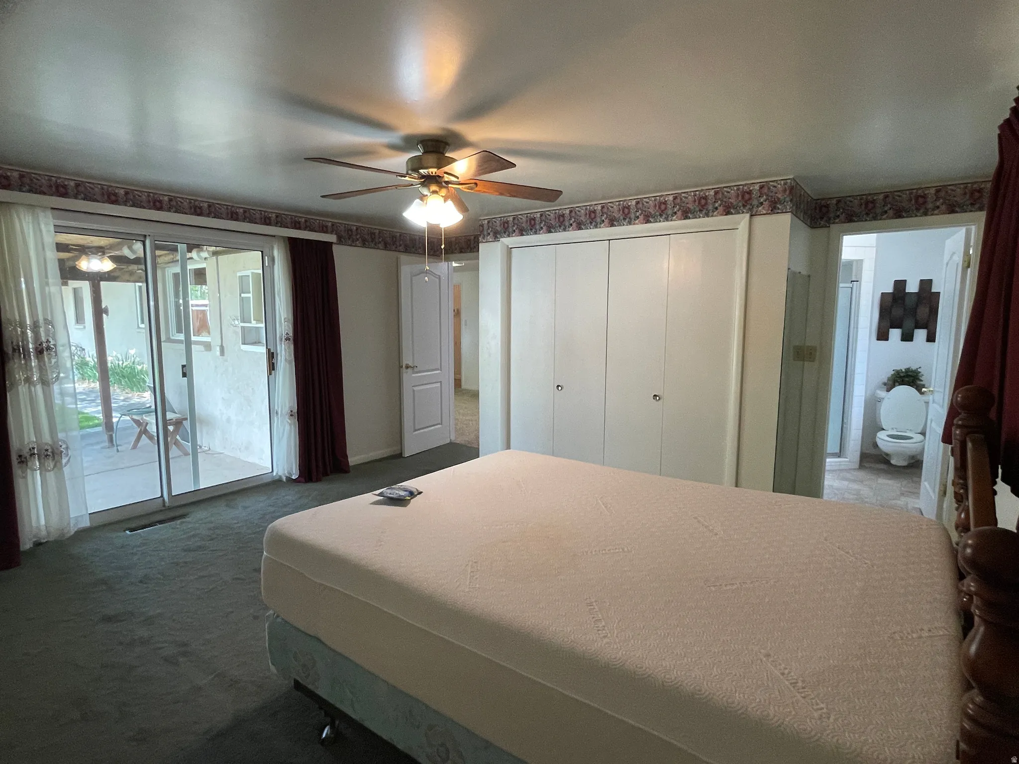 Primary bedroom with private bath and sliding glass doors opening to an exterior patio, a white bi-fold closet, and a doorway revealing a bathroom.