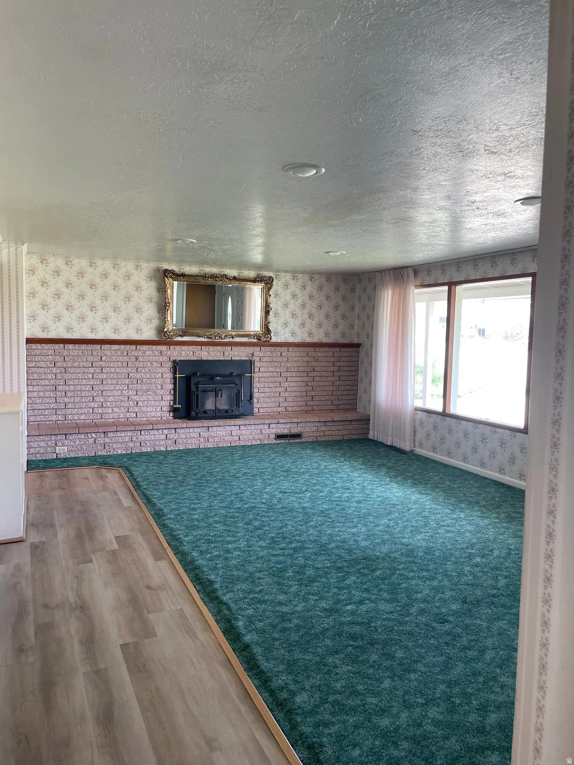 Spacious room featuring a brick fireplace with a dark insert, large windows, recessed lighting, wood-finish flooring, and wall-to-wall carpeting