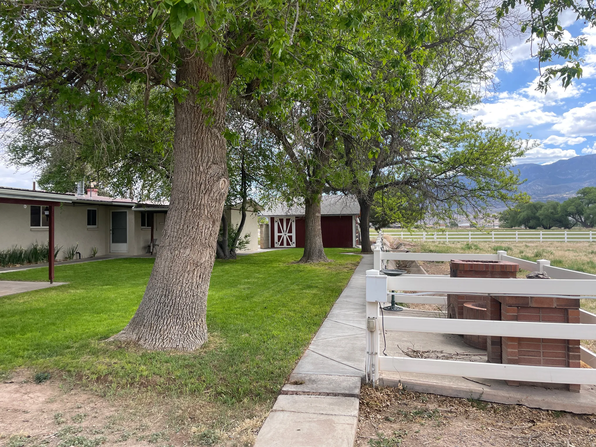 Expansive property featuring a manicured lawn, established shade trees, a white picket fence, and a distant mountain backdrop