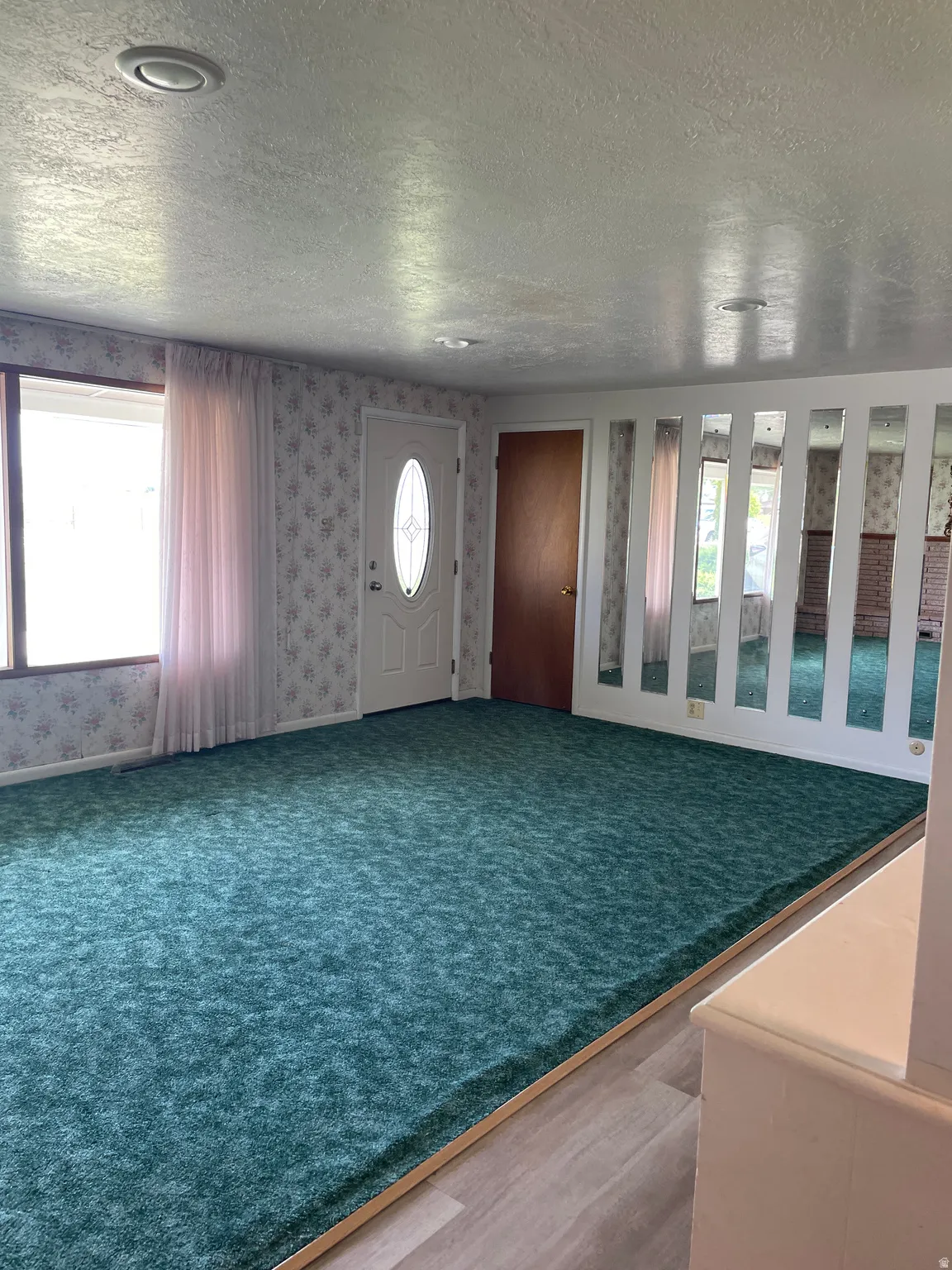 Spacious interior room featuring plush green carpeting and light wood-finish flooring