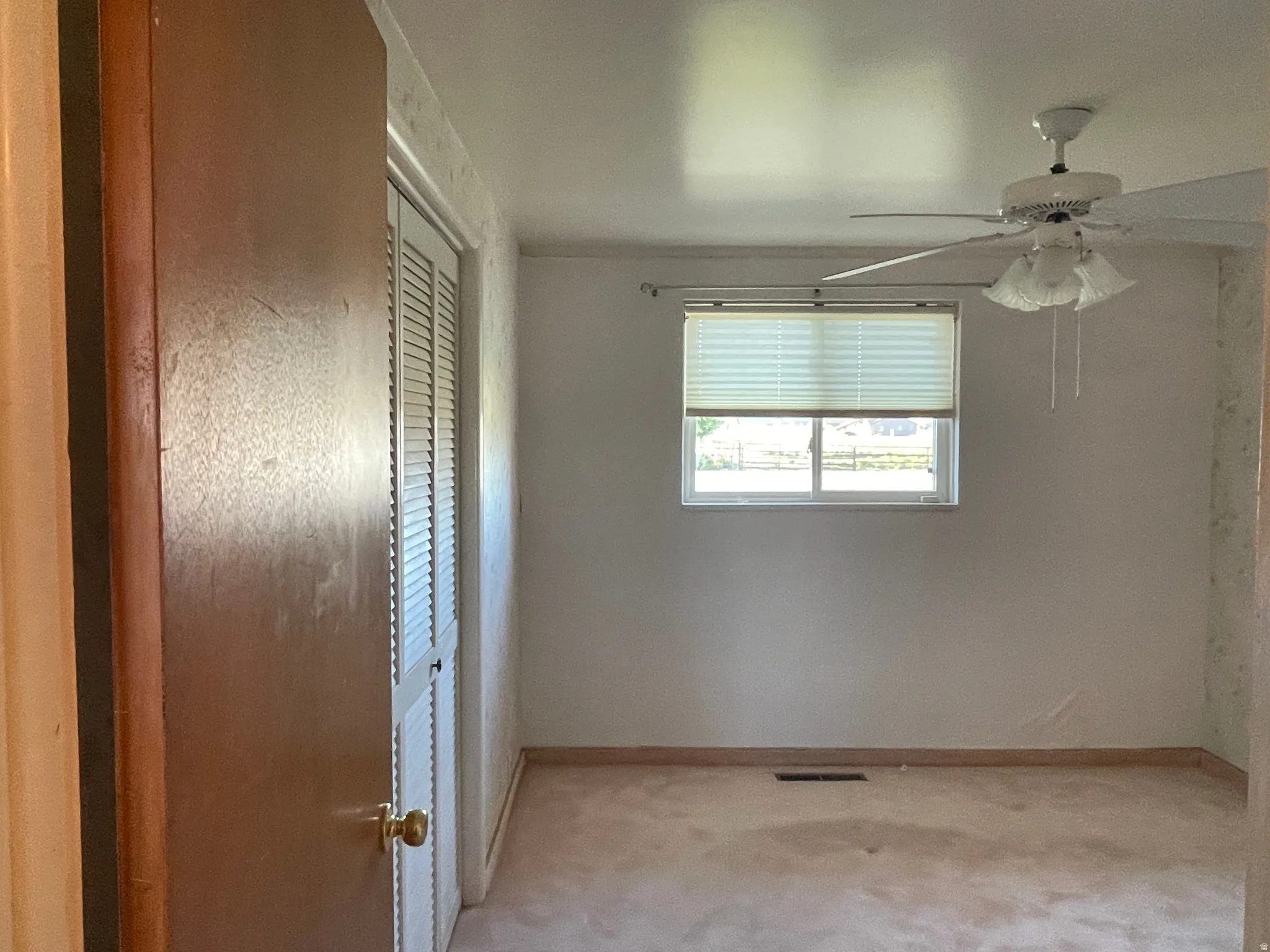 Interior room featuring a ceiling fan with integrated lighting, a window with horizontal blinds, carpet flooring, and a louvered bi-fold closet door