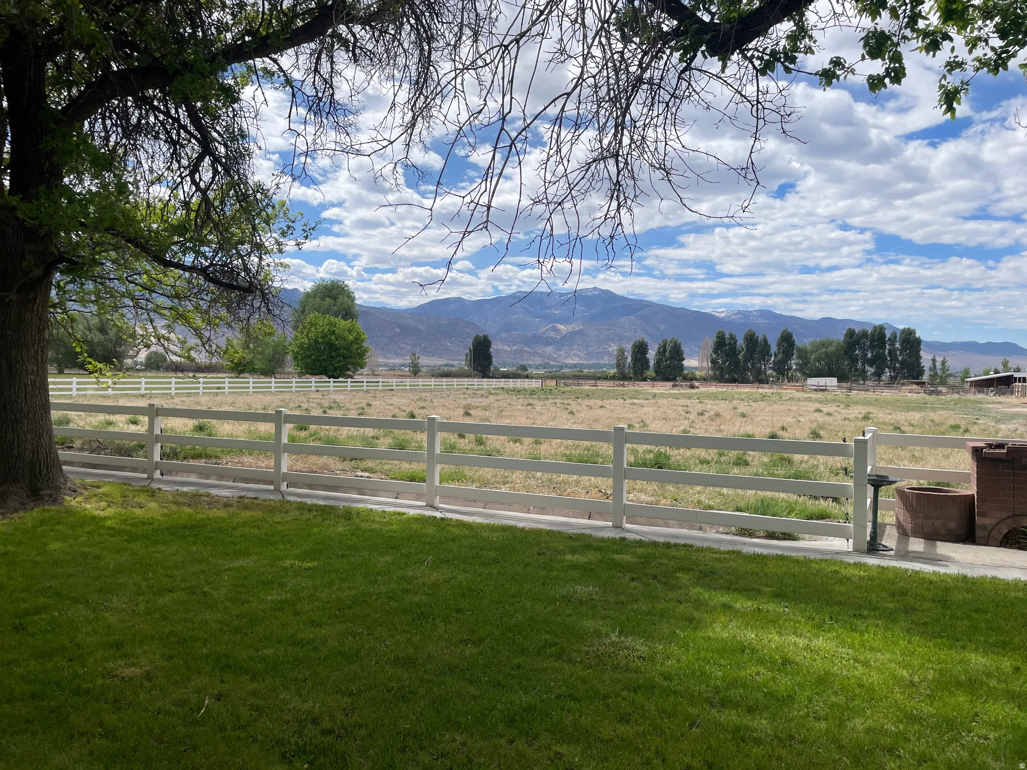 Expansive outdoor space featuring a manicured lawn, white perimeter fencing, and distant mountain scenery under a cloudy sky