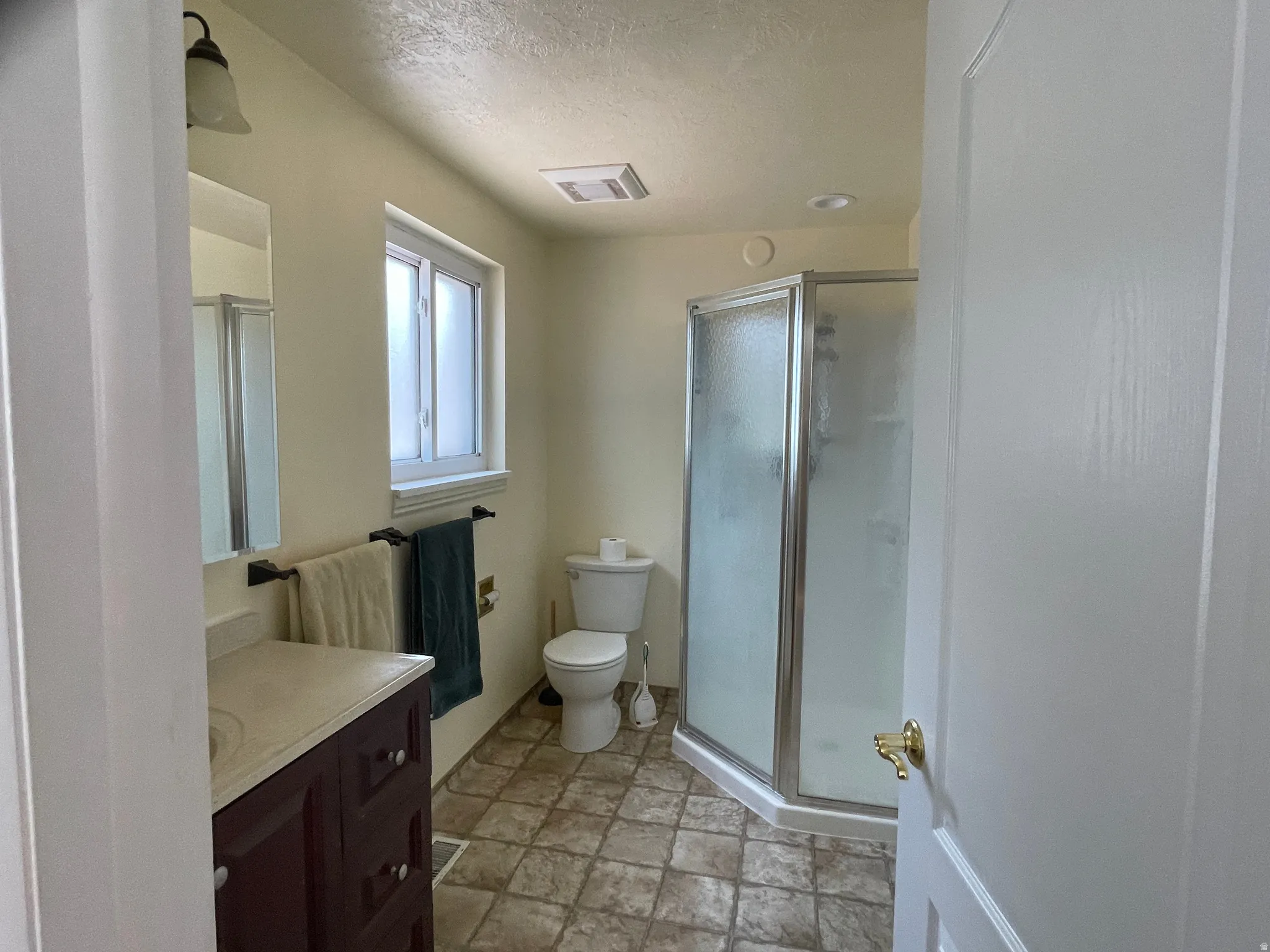 Bathroom featuring a glass-enclosed shower, a vanity with a light-colored countertop, and a window with white trim