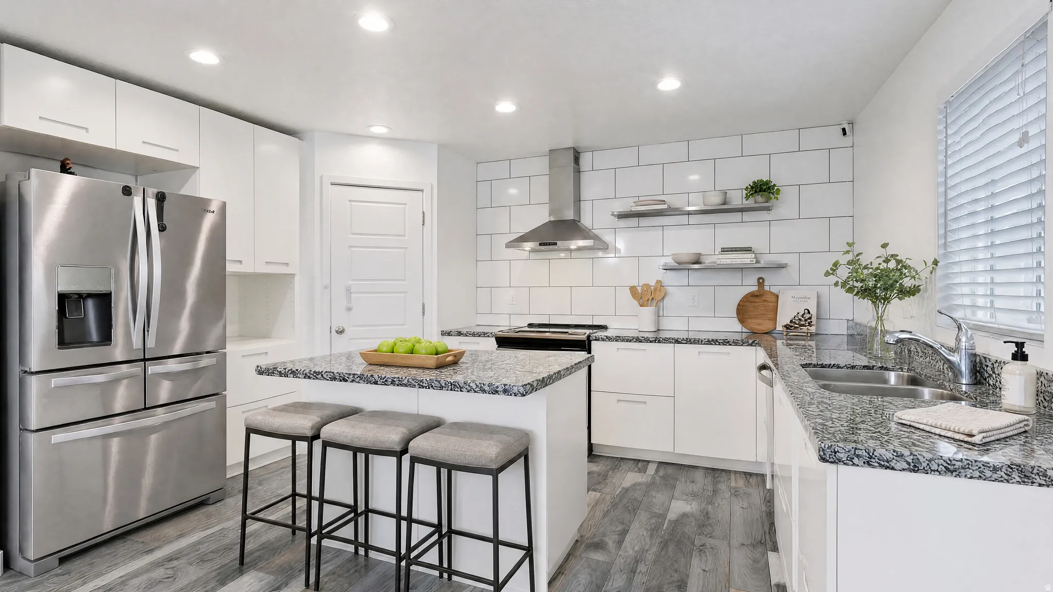 Virtually Staged | Contemporary kitchen featuring a center island with countertop seating, granite countertops, stainless steel appliances, white subway tile backsplash, and wood-finish flooring