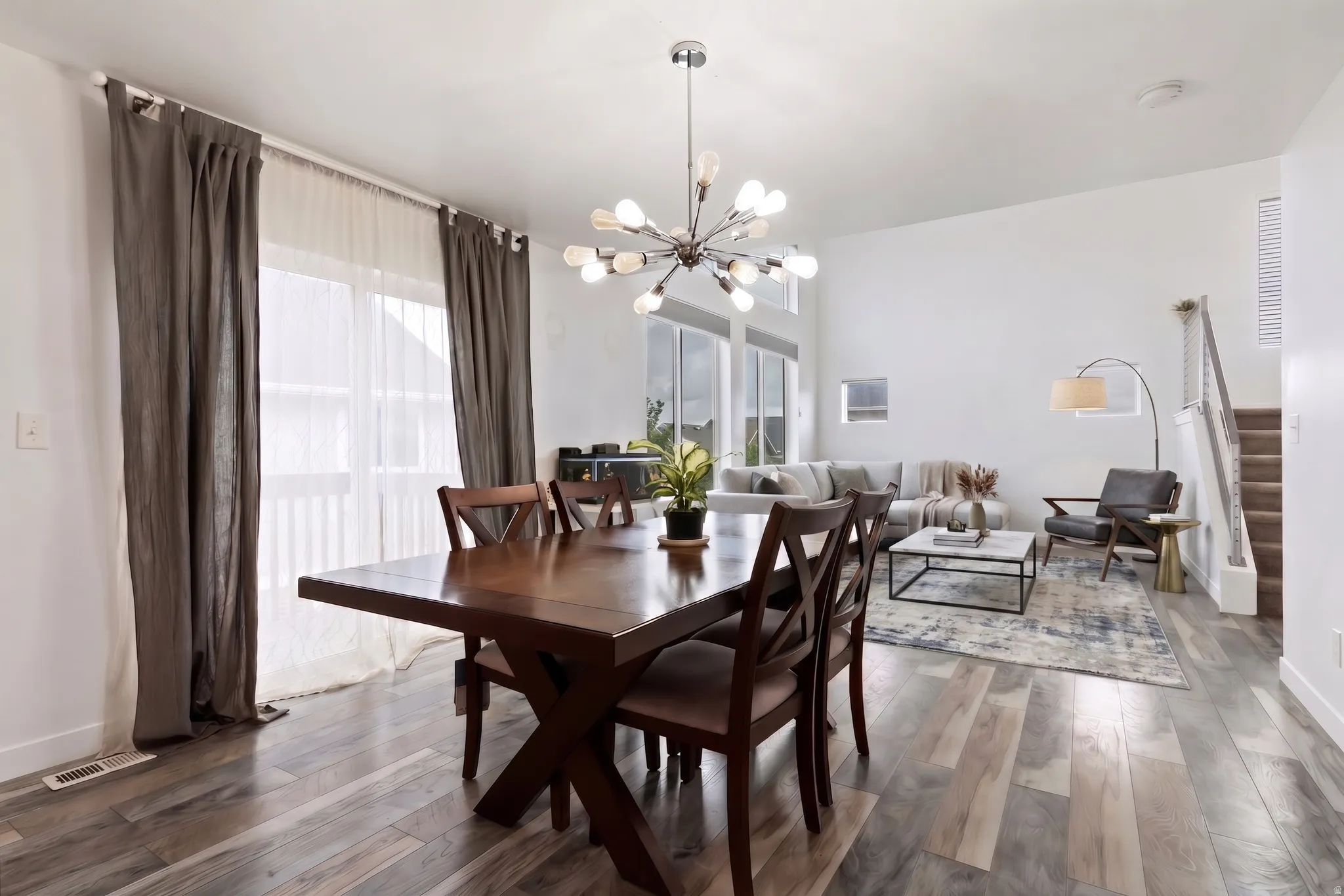 Virtually Staged | Spacious dining area featuring a modern chandelier, wood-finish flooring, and large windows providing abundant natural light