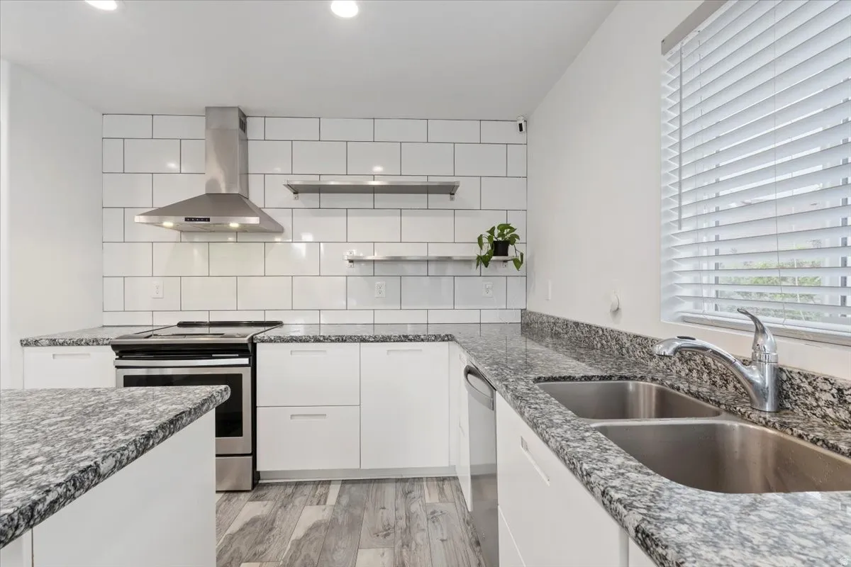 Kitchen featuring granite countertops, a subway tile backsplash, stainless steel appliances, white cabinetry, and wood-finish flooring