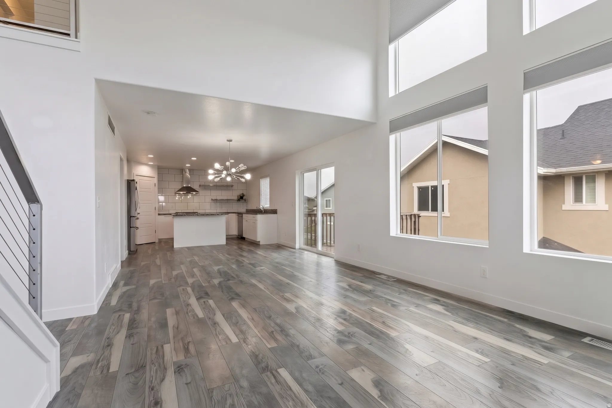Virtually Staged | Open-concept living space featuring wood-finish flooring, high ceilings, tall windows with integrated shades, a modern kitchen with a central island, and a sliding glass door to an exterior deck