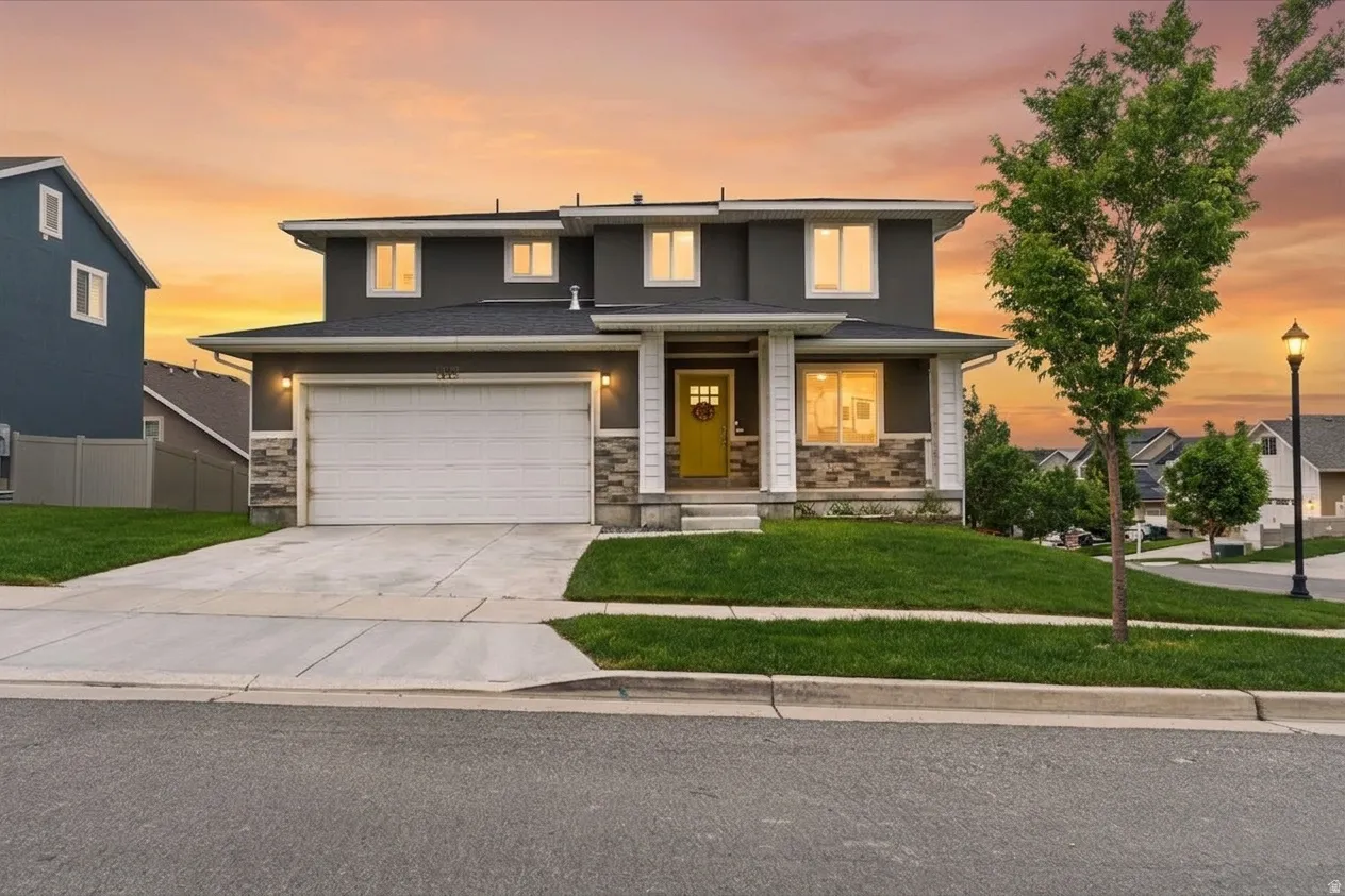 Contemporary two-story residence featuring a two-car garage, stone façade accents, a covered front porch, and a vibrant yellow front door