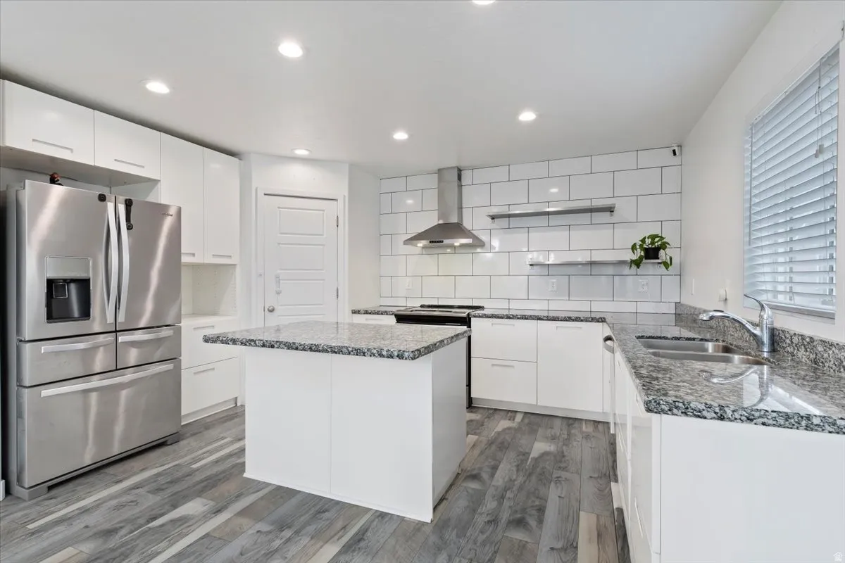 Kitchen featuring a central island with a granite countertop, white flat-panel cabinetry, stainless steel appliances, and wood-finish flooring