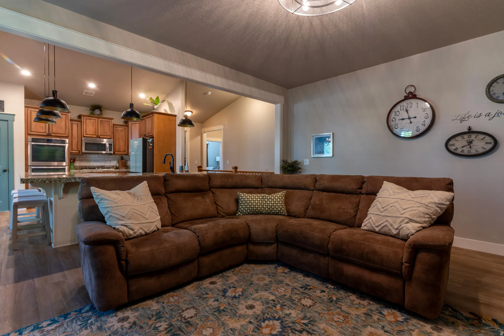 Open-concept living area featuring wood-finish flooring and a kitchen with warm wood cabinetry, stainless steel appliances, and a built-in oven
