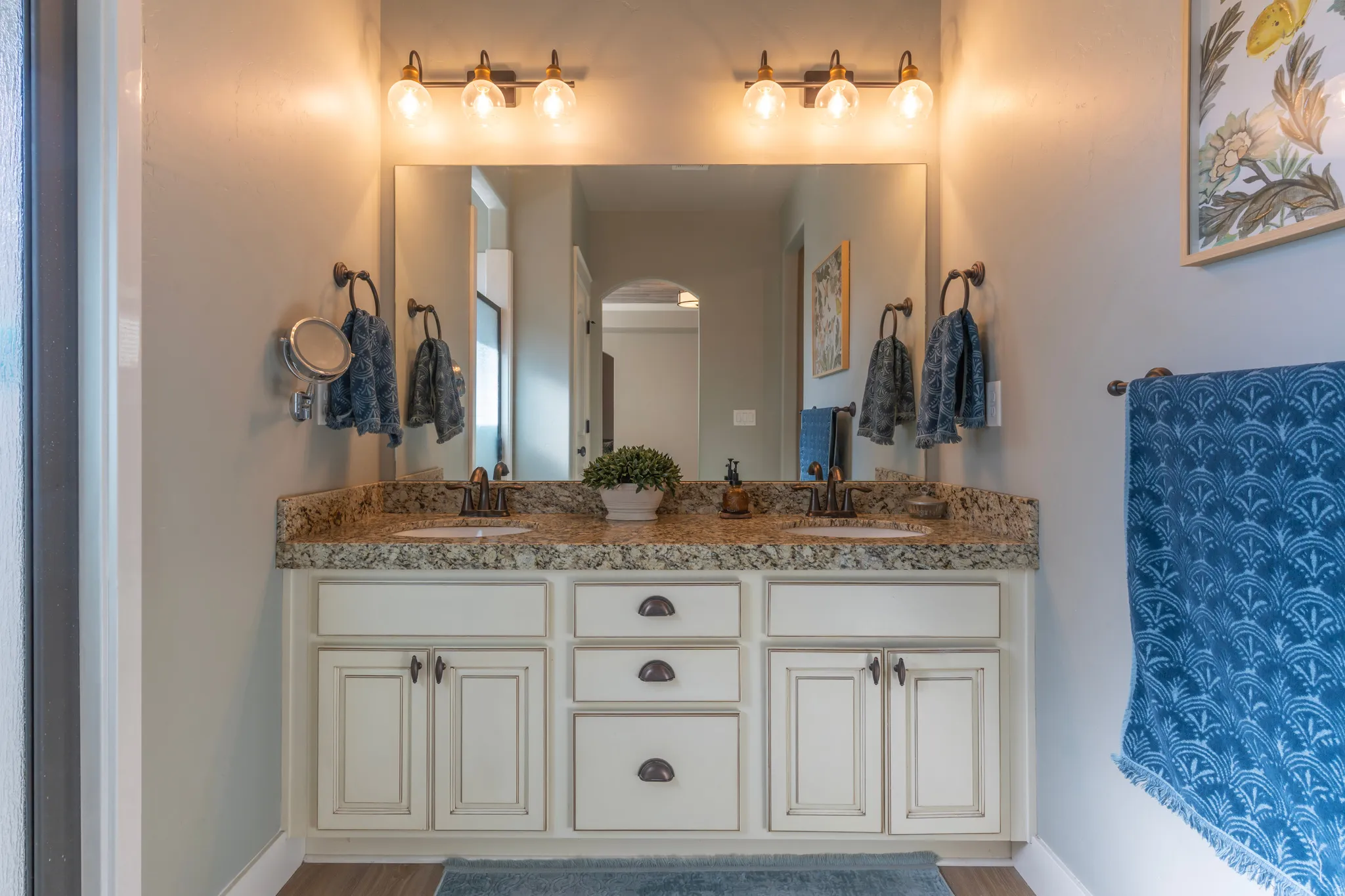 Double vanity featuring a granite countertop with two undermount sinks, bronze faucets, and antique white cabinetry with bronze hardware