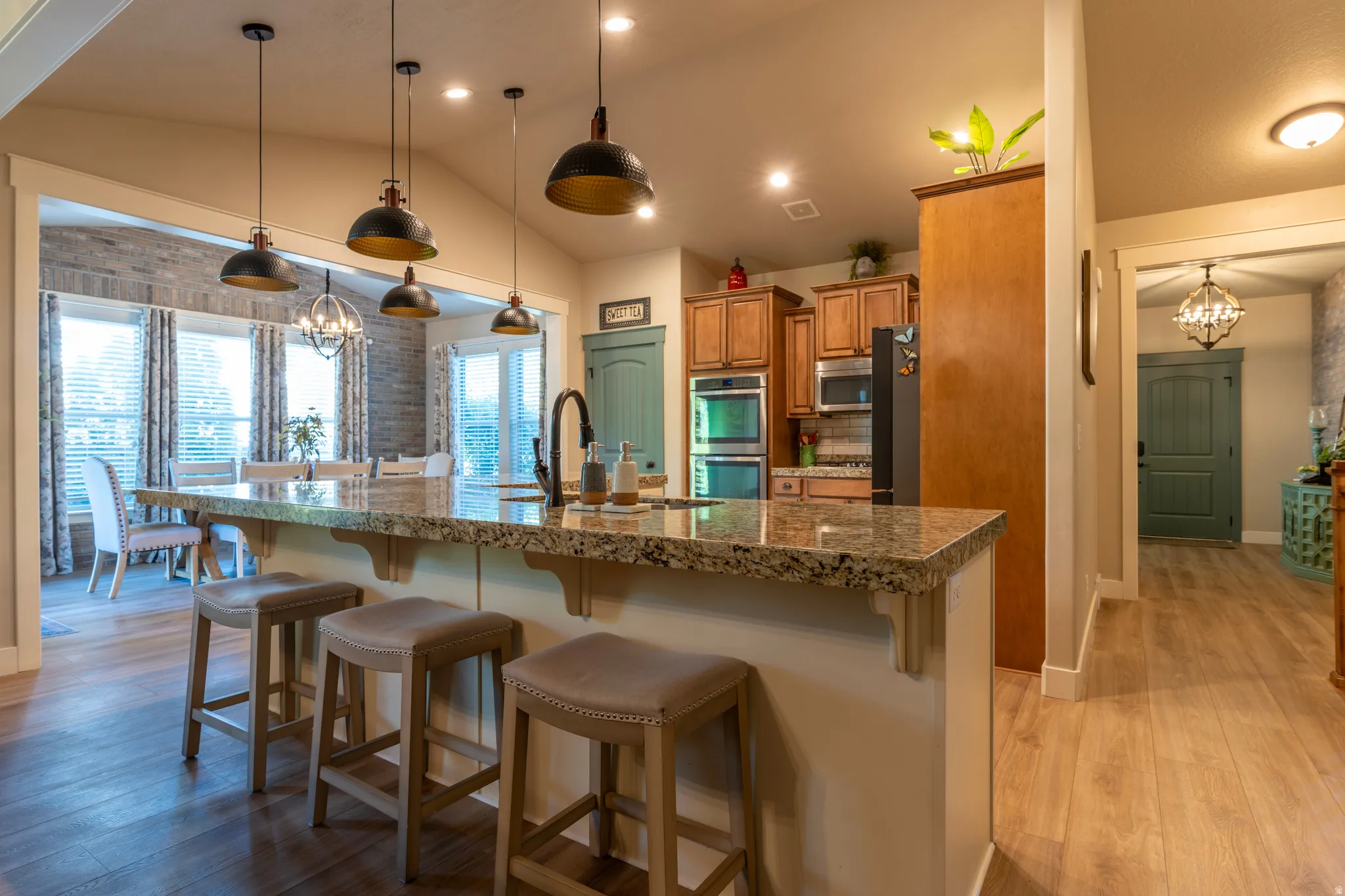 Open-concept kitchen featuring an expansive island with a granite countertop, pendant lighting, built-in double ovens, and wood-finish flooring