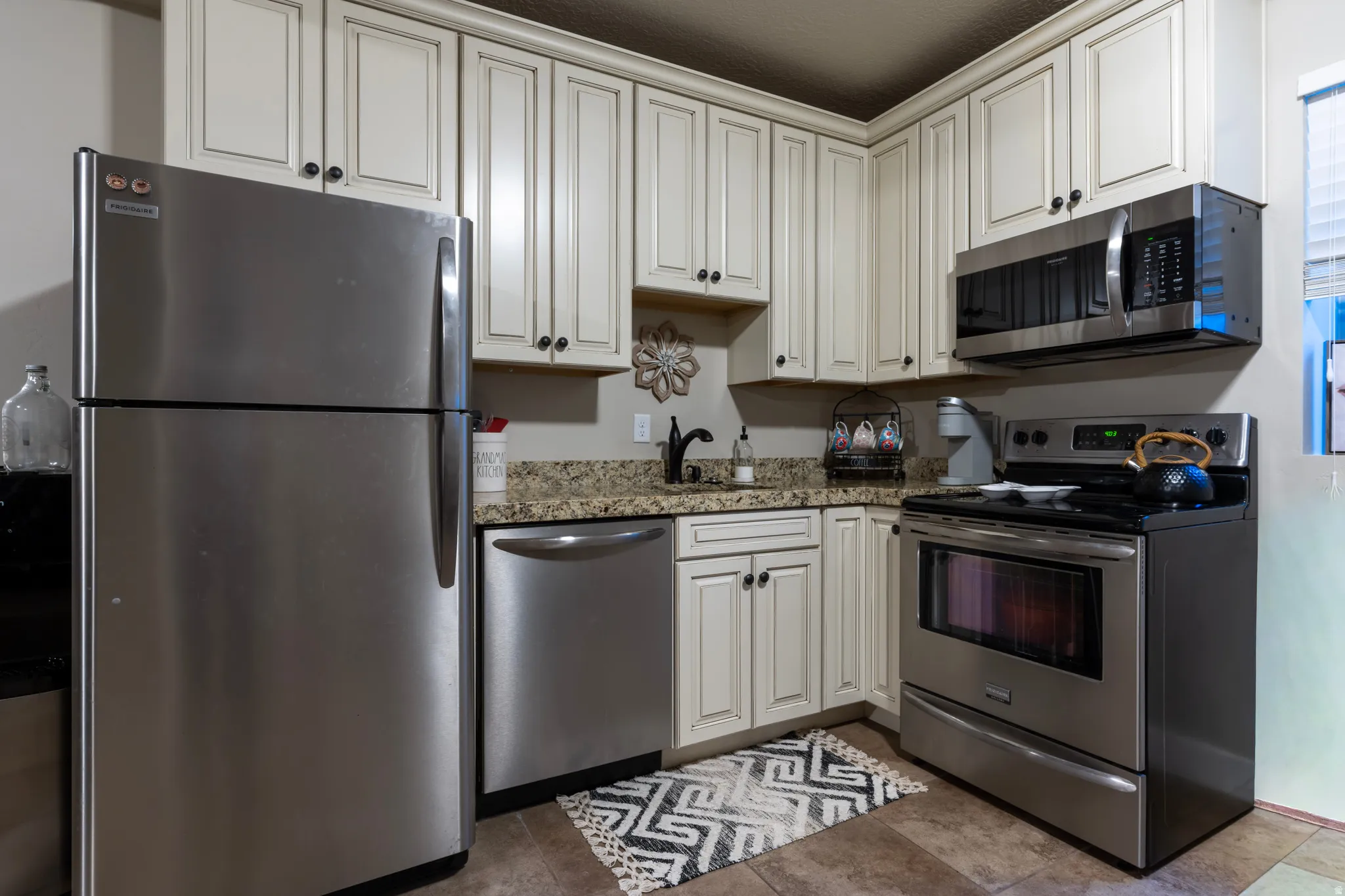 Kitchen featuring stainless steel appliances, extensive cream-colored cabinetry with dark hardware, a granite-finish countertop, and a built-in microwave
