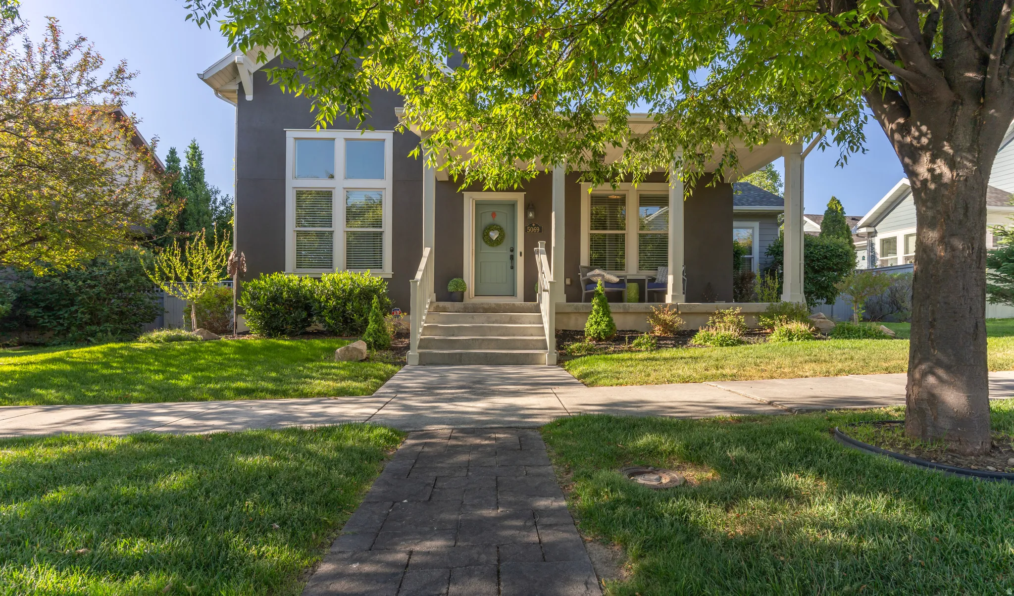 Charming two-story residence featuring a covered front porch with white columns, a light blue entry door, and a paver stone walkway