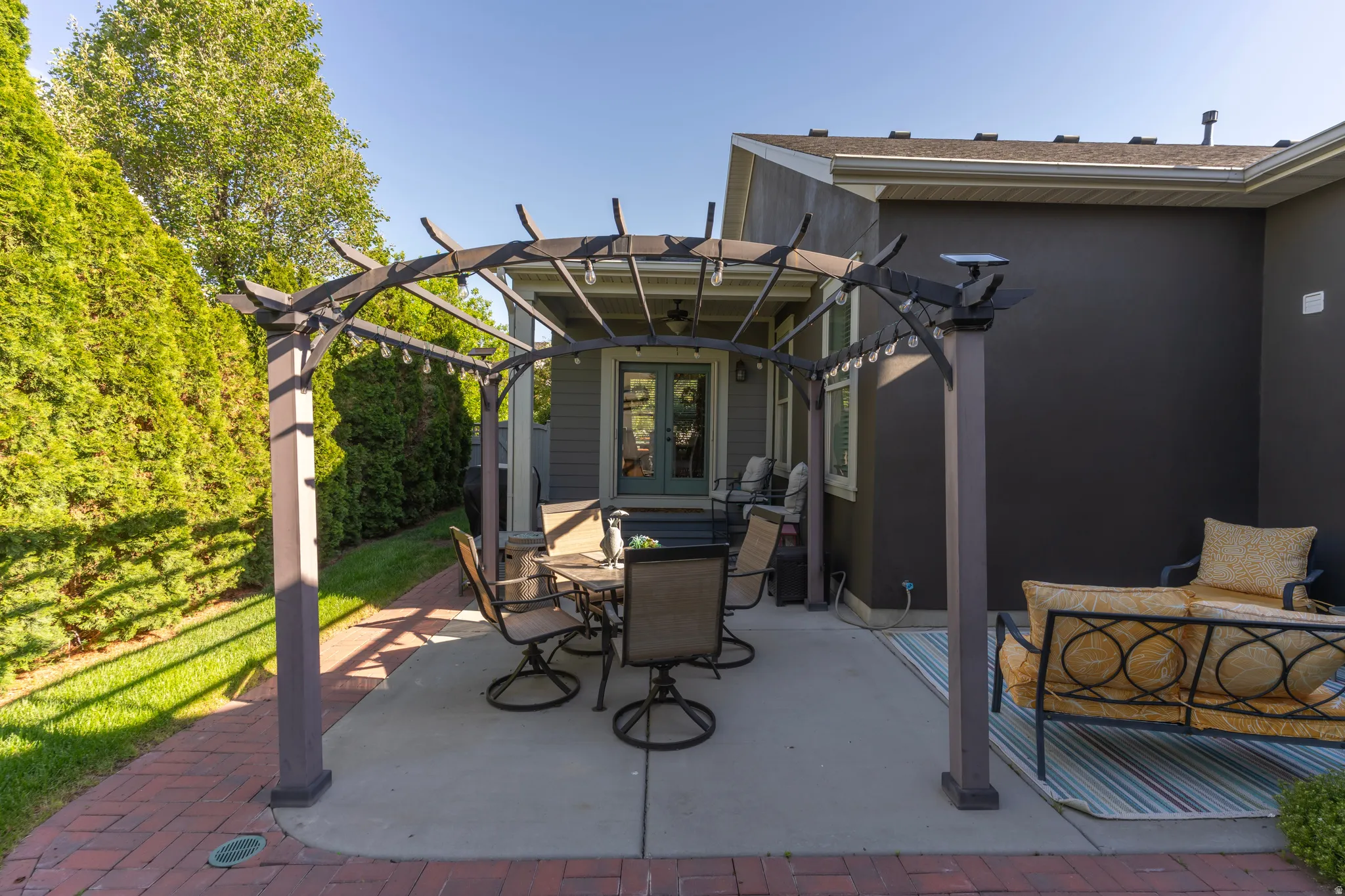 Outdoor patio featuring a dark wood pergola, concrete slab, brick paver accents, and direct access to the interior via double doors