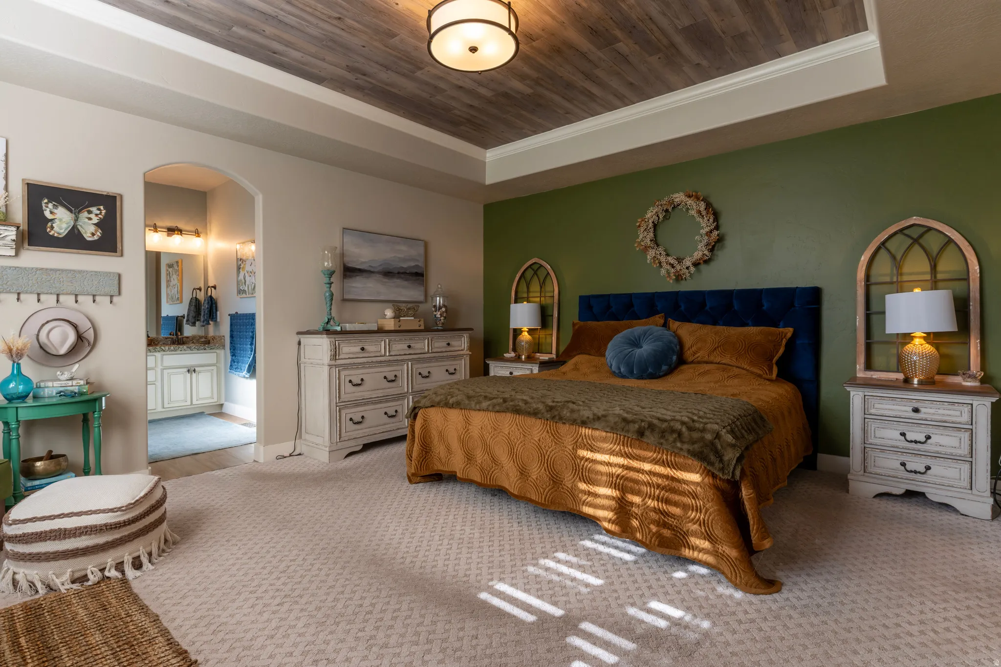 Spacious bedroom featuring a tray ceiling with wood-finish paneling, an arched entryway to the bathroom, and neutral carpeting