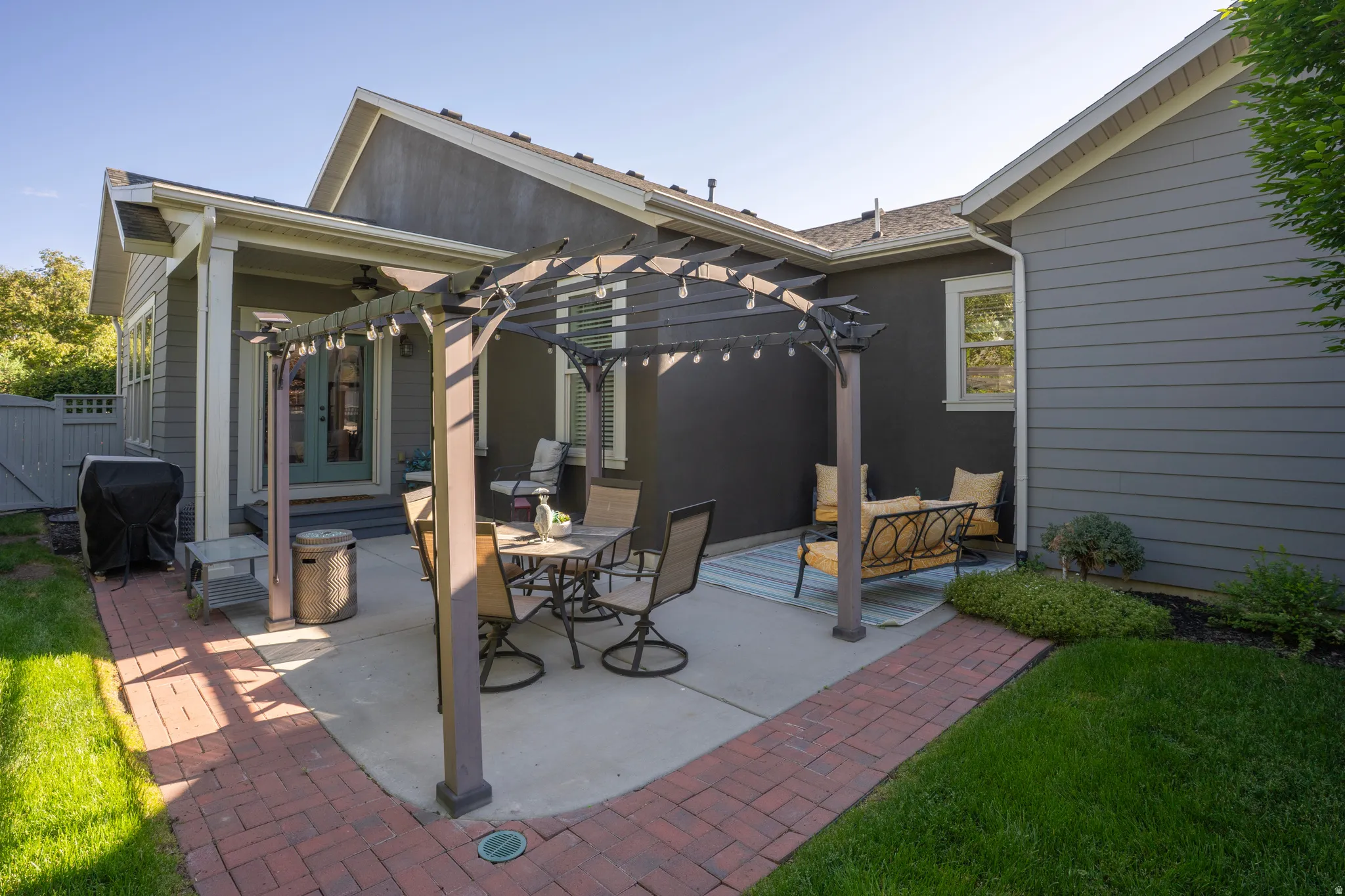 Expansive concrete patio featuring a wood pergola and brick paver walkway