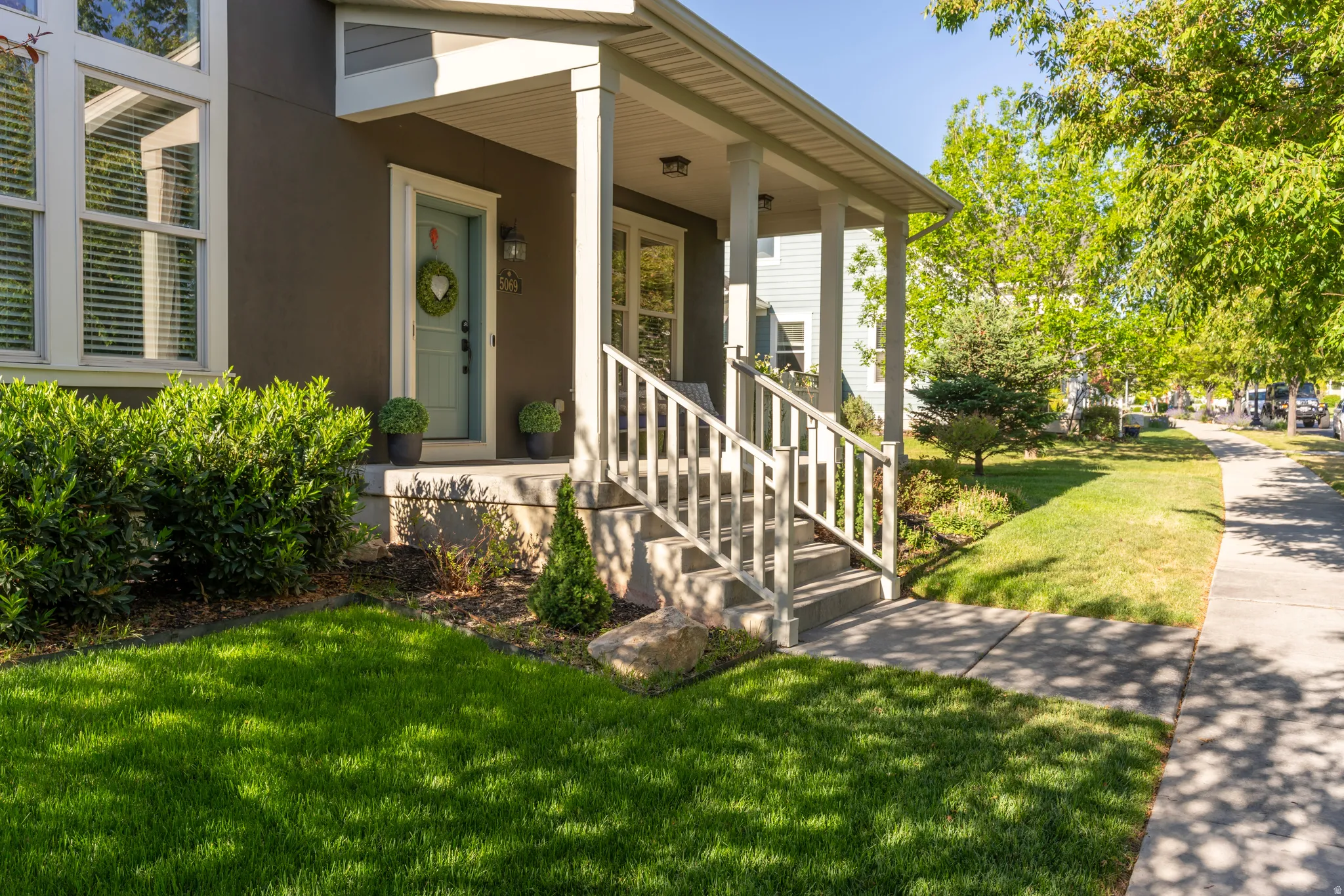 Inviting front porch with white columns and railings, offering concrete steps to a well-maintained lawn and sidewalk
