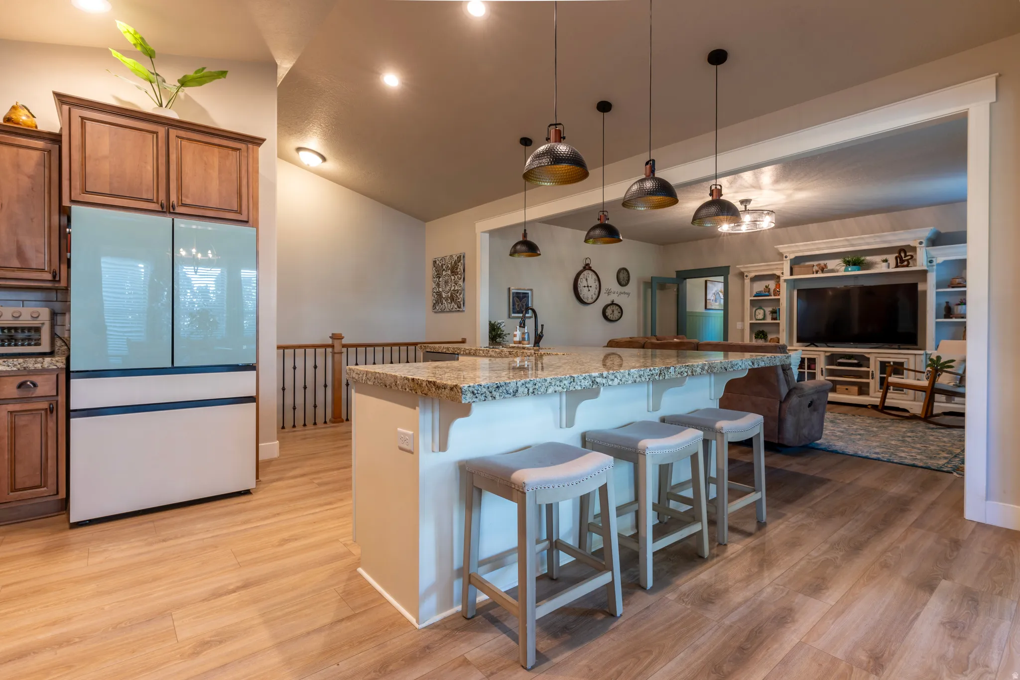 Open-concept kitchen and living area featuring a large island with stone countertop, pendant lighting, wood-finish flooring, and warm-toned cabinetry